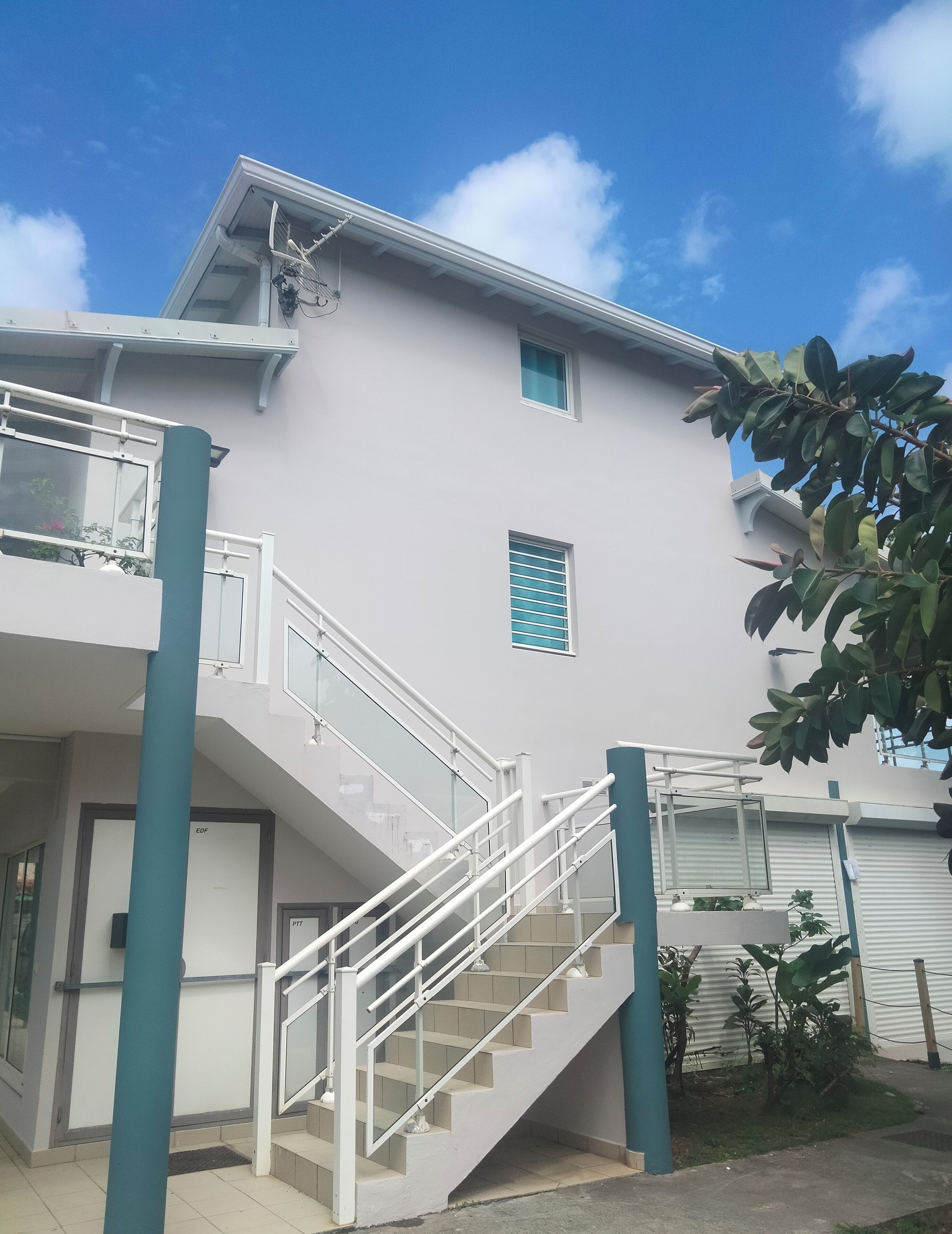 A modern building with a white exterior, a staircase leading to a balcony, and a small window with blue shutters.