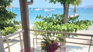 Mesa de comedor preparada para cuatro con sillas rojas, un florero y vista al mar con barcos.