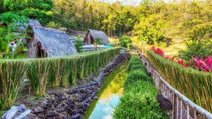 Un pueblo rústico con chozas de techo de paja, un estrecho canal de agua y abundante vegetación.