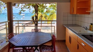 Un balcón con una mesa y sillas de madera, vista a la playa y al océano, y una cocina con gabinetes color naranja.