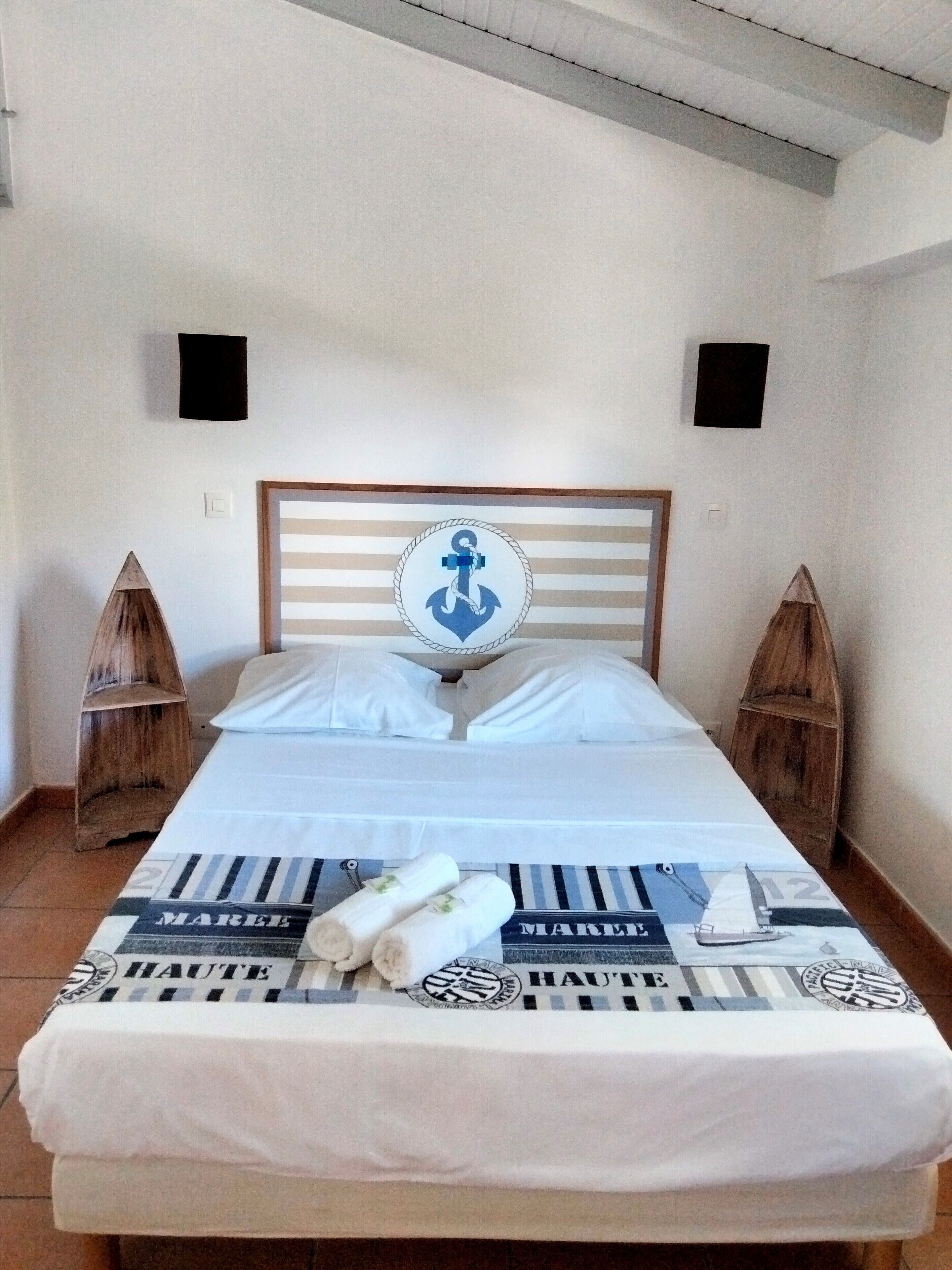 Een bed met een gestreept hoofdeinde, twee houten nachtkastjes en een bedspreide in een nautisch thema.