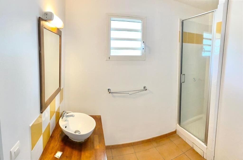 A bathroom with a sink, mirror, window, towel rack, and glass shower enclosure.