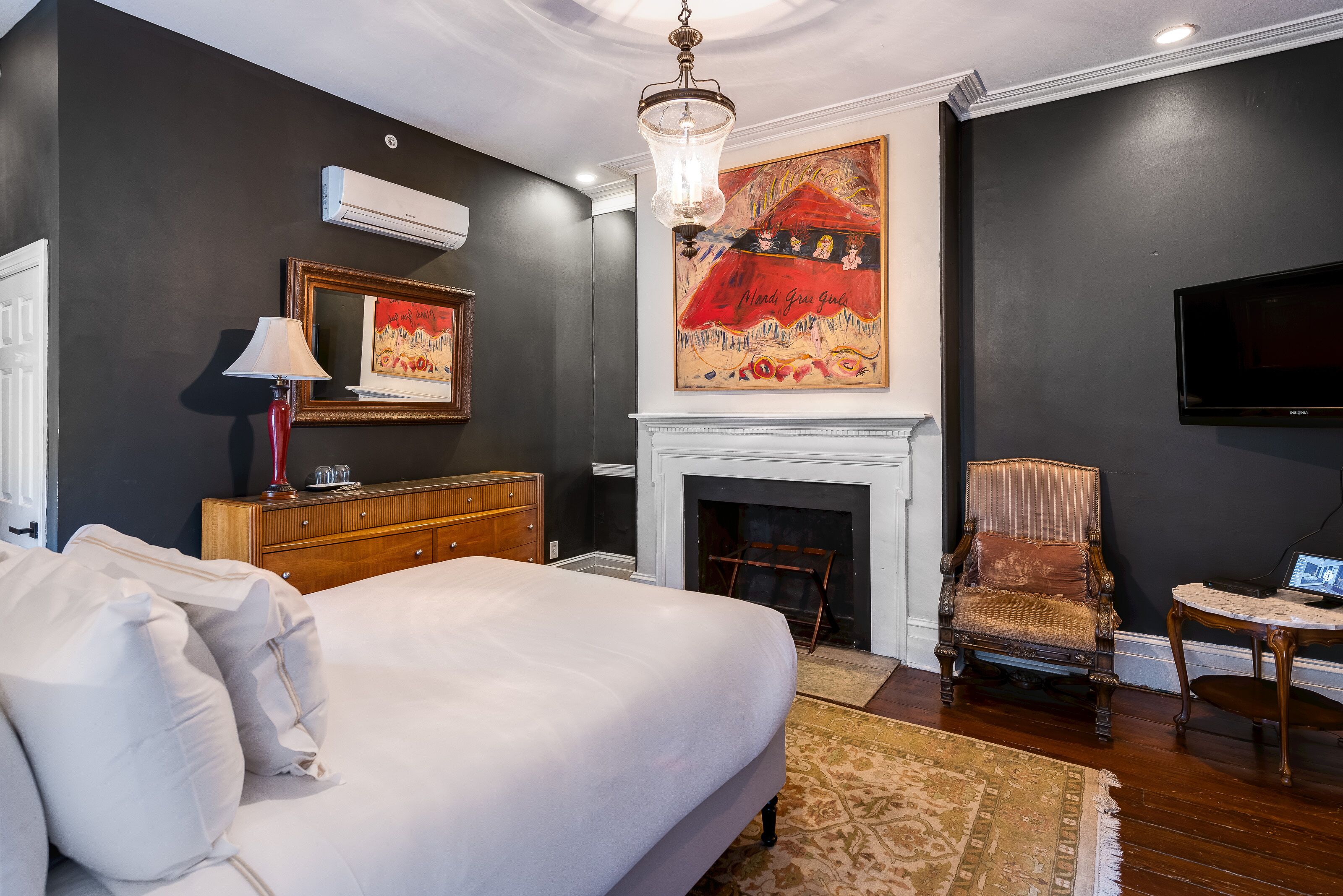 A bedroom with a large bed, a fireplace, a television, and a painting on the wall.