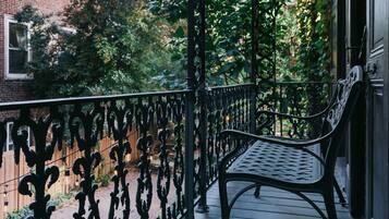 A wooden balcony with a wrought iron railing and a bench.