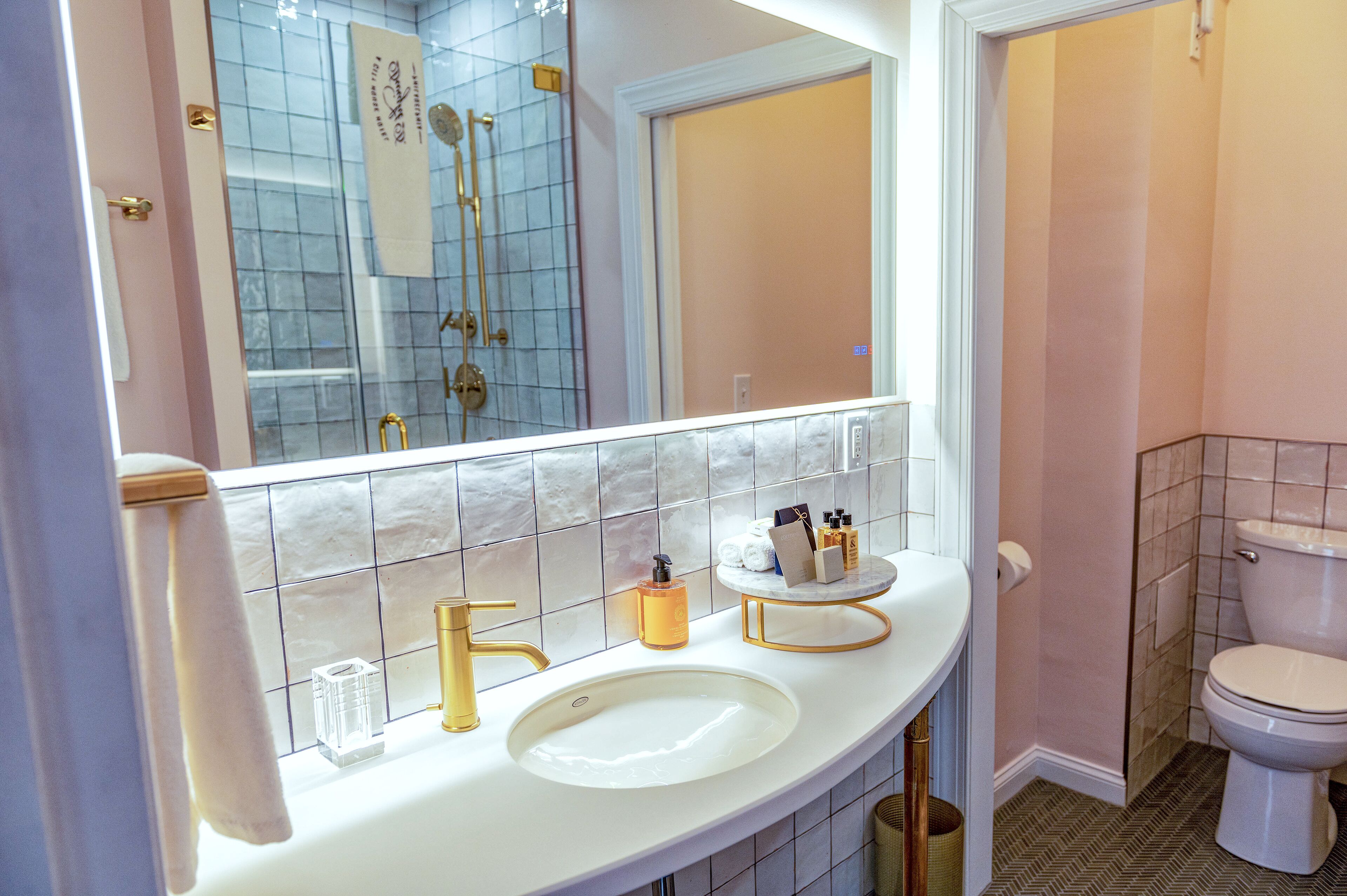 A bathroom with a white sink, gold faucet, and a large mirror.