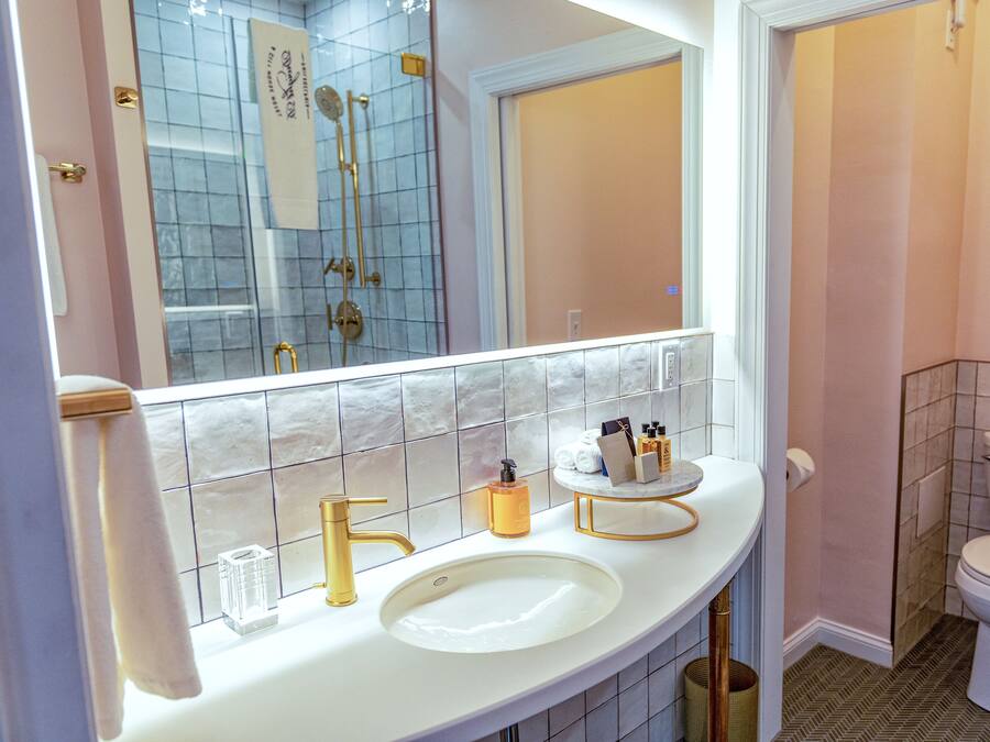 A bathroom with a white sink, gold faucet, and a large mirror.