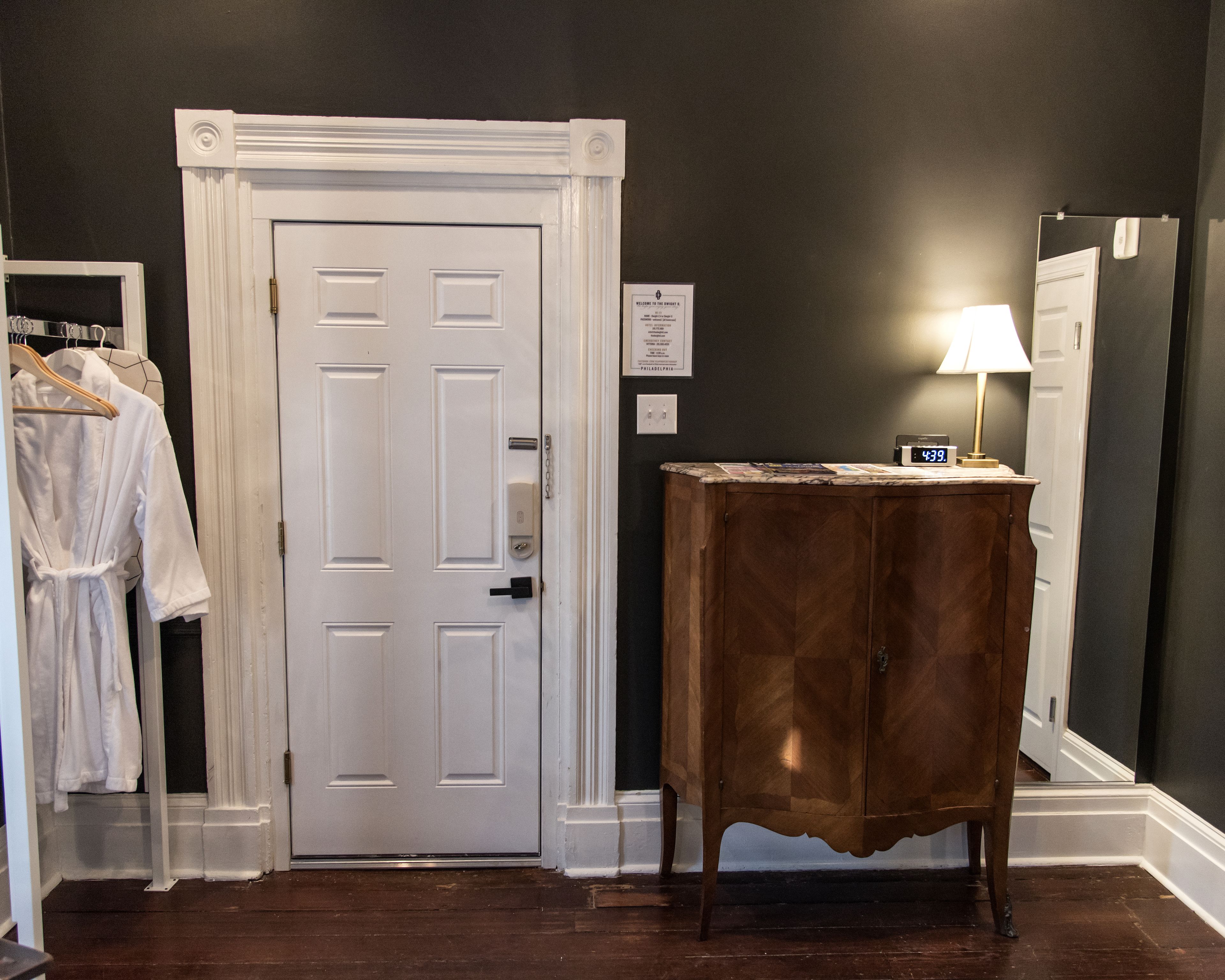 A room with a white door, a wooden cabinet, a mirror, and a clock on the cabinet.