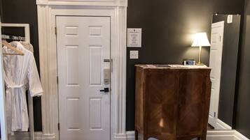 A room with a white door, a wooden cabinet, a mirror, and a clock on the cabinet.
