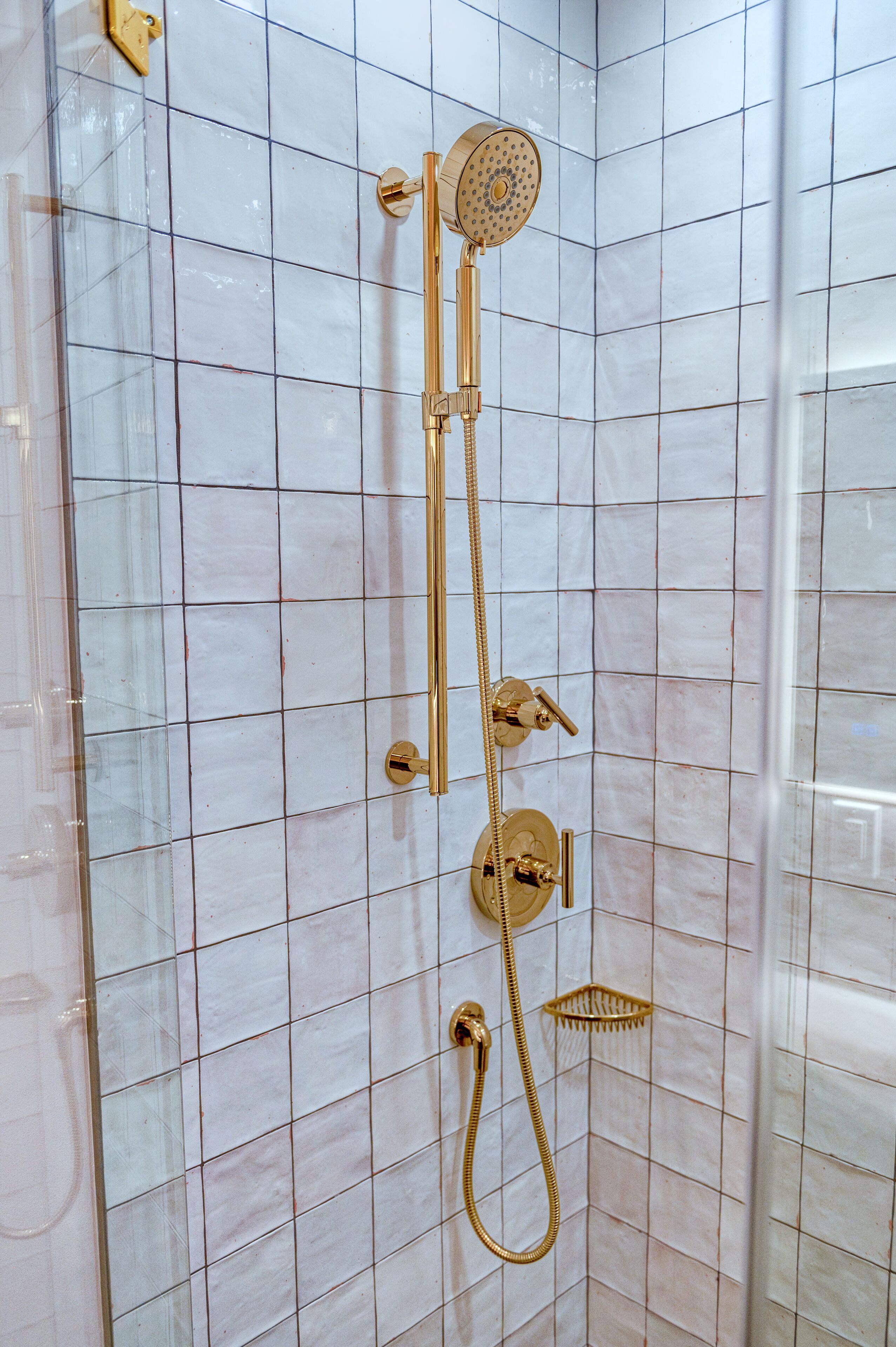 A shower with a gold showerhead and control panel, set against a tiled wall.