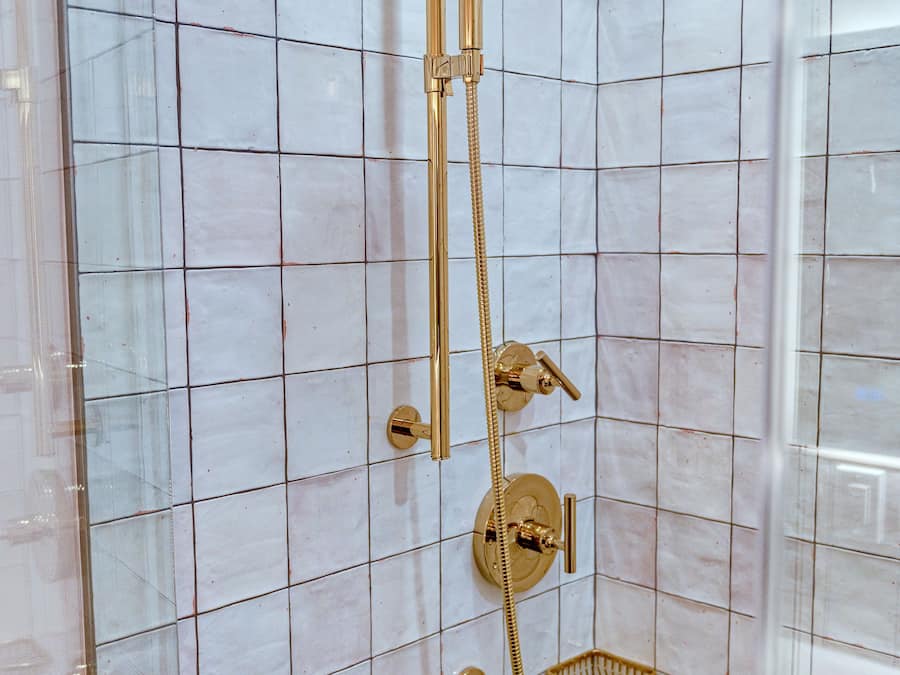 A shower with a gold showerhead and control panel, set against a tiled wall.
