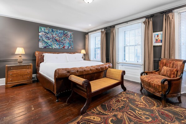A bedroom with a large bed, a wooden nightstand, a chair, and a patterned rug.