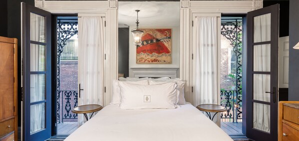 Habitación de hotel con una cama grande, dos mesitas de noche, un cuadro en la pared y un balcón con vistas a la ciudad.