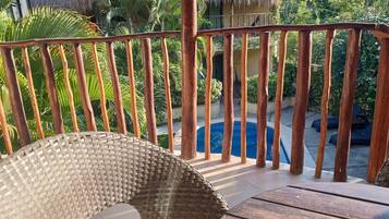 Una terraza de madera con una silla de mimbre, una piscina y una estructura con techo de paja al fondo.