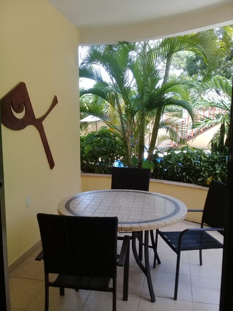Un comedor con una mesa redonda y cuatro sillas, un adorno en la pared y vistas a un exuberante jardín con palmeras.