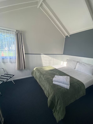 A hotel room with a bed, a chair, a window with curtains, and a view of greenery outside.