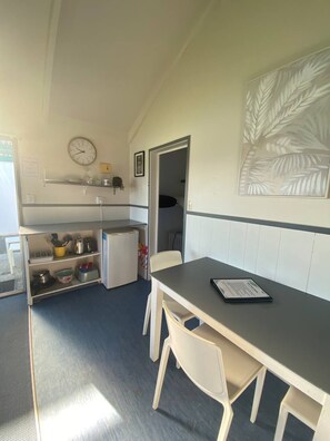A compact kitchen with a refrigerator, a clock, and a dining table with chairs.
