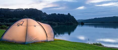 Tenda abobadada montada numa colina gramada, com vista para um lago calmo e colinas arborizadas ao fundo.