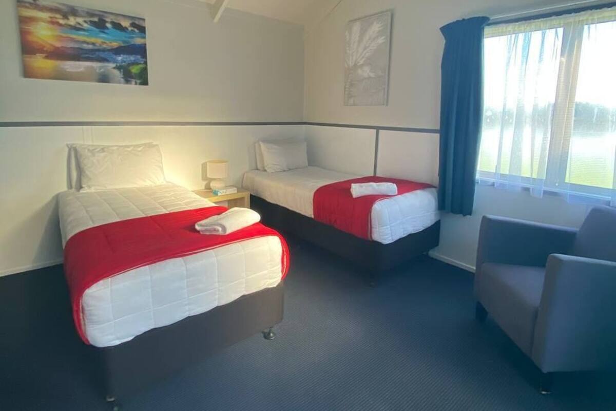 A hotel room with two beds, a chair, a nightstand, and a window with curtains.