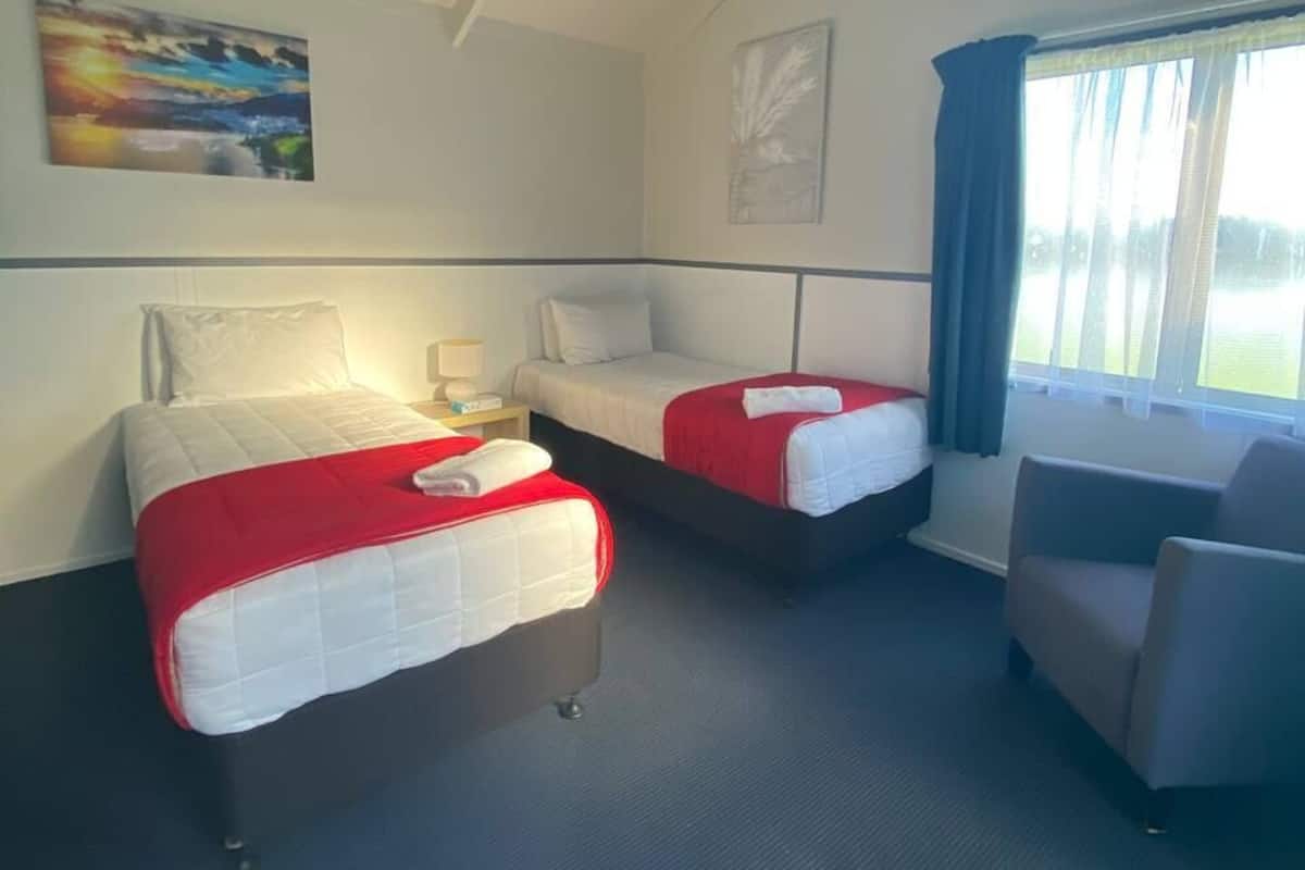 A hotel room with two beds, a chair, a nightstand, and a window with curtains.