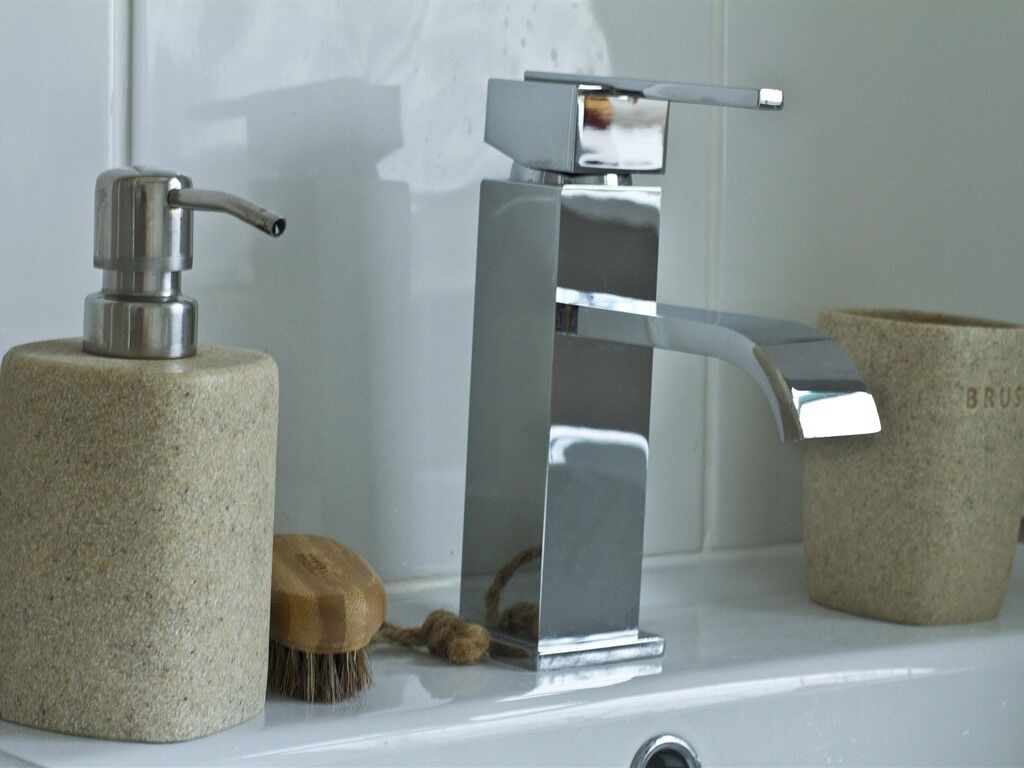 A bathroom with a modern faucet, a soap dispenser, and a wooden brush.