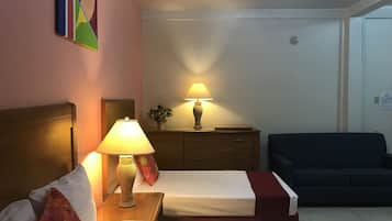 Habitación de hotel con dos camas, una mesita de noche con lámpara, un aparador, un sofá y un cuadro en la pared.