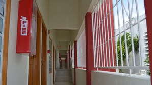 A corridor with red and white walls, a fire exit sign, and barred windows. - Alicia's Inn (Philipsburg)
