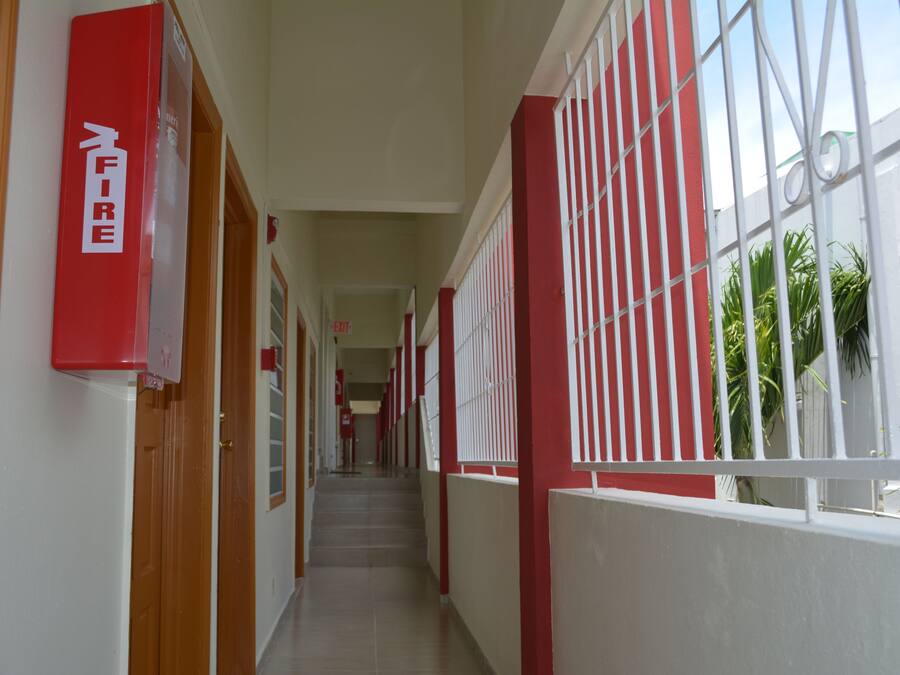 Un couloir aux murs rouges et blancs, une signalisation indiquant la sortie de secours et des fenêtres grillagées.