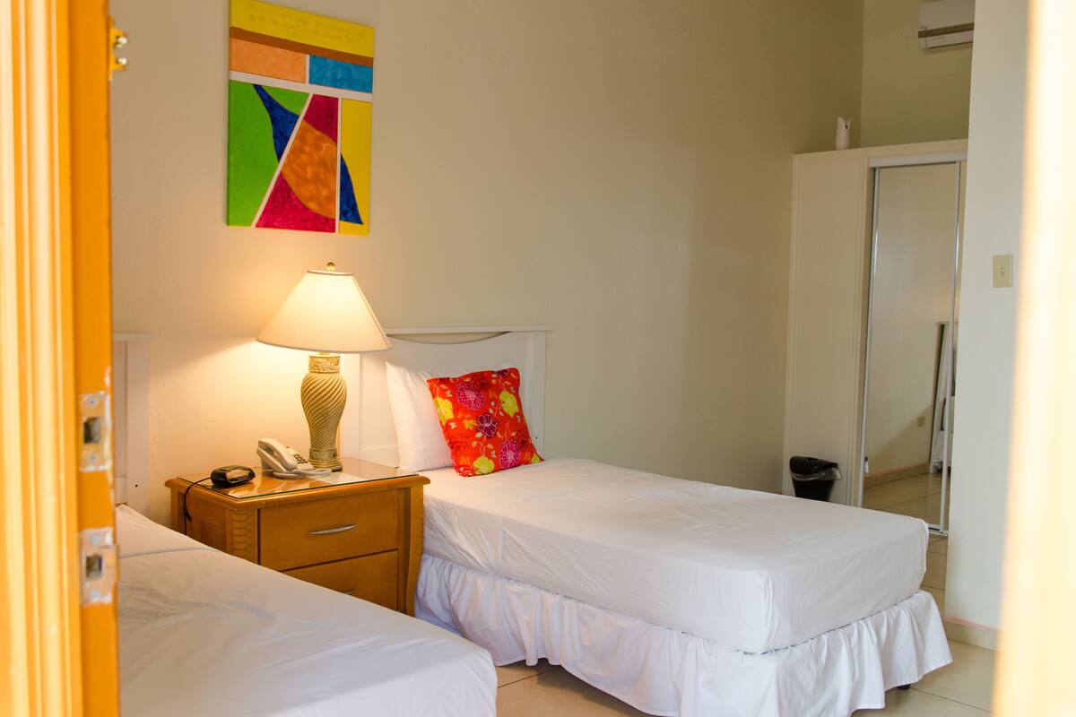 Une chambre d’hôtel avec deux lits, une lampe de chevet, un téléphone et une œuvre d’art colorée accrochée au mur.
