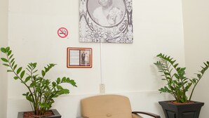A beige armchair in a room with a white wall, an exit sign, a framed picture, and two potted plants. - Alicia's Inn (Philipsburg)