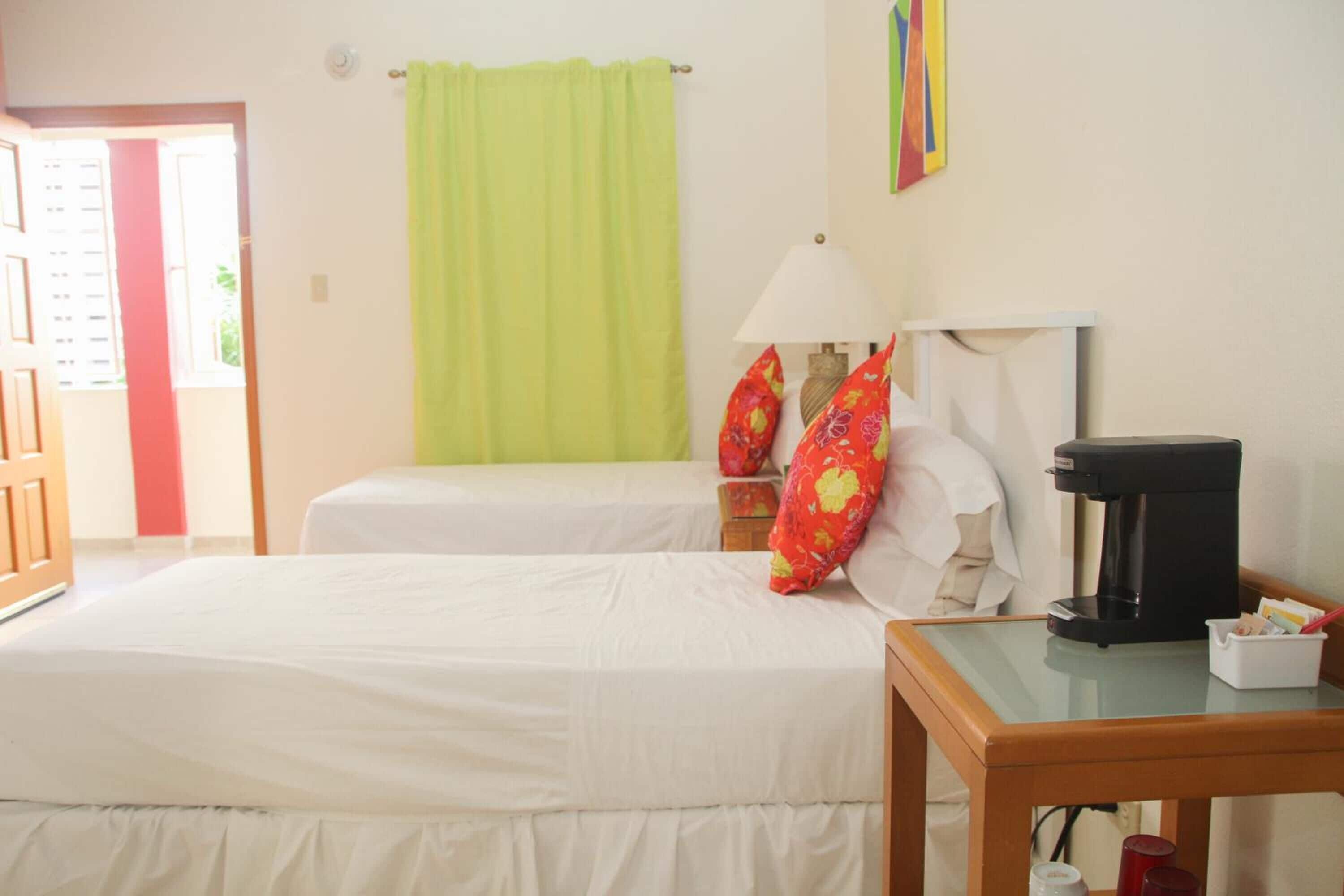 Quarto de hotel com duas camas, uma cafeteira e um abajur sobre uma mesa de madeira.