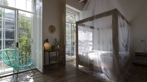 Un dormitorio con cama con dosel, una silla, un escritorio y vistas al exterior.