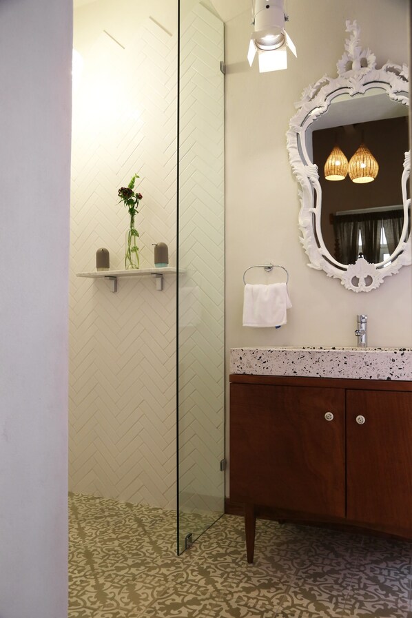 A bathroom with a glass shower enclosure, a wooden vanity with a mirror, and a patterned floor. - El Patio 77 (Mexico City)