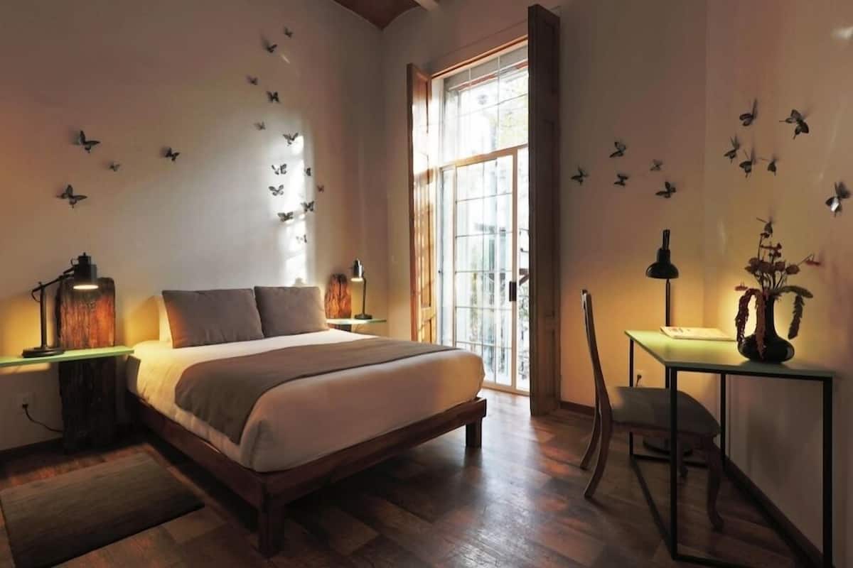 A bedroom with a large bed, a desk, and a chair. There are butterfly decals on the walls and a window with a view.