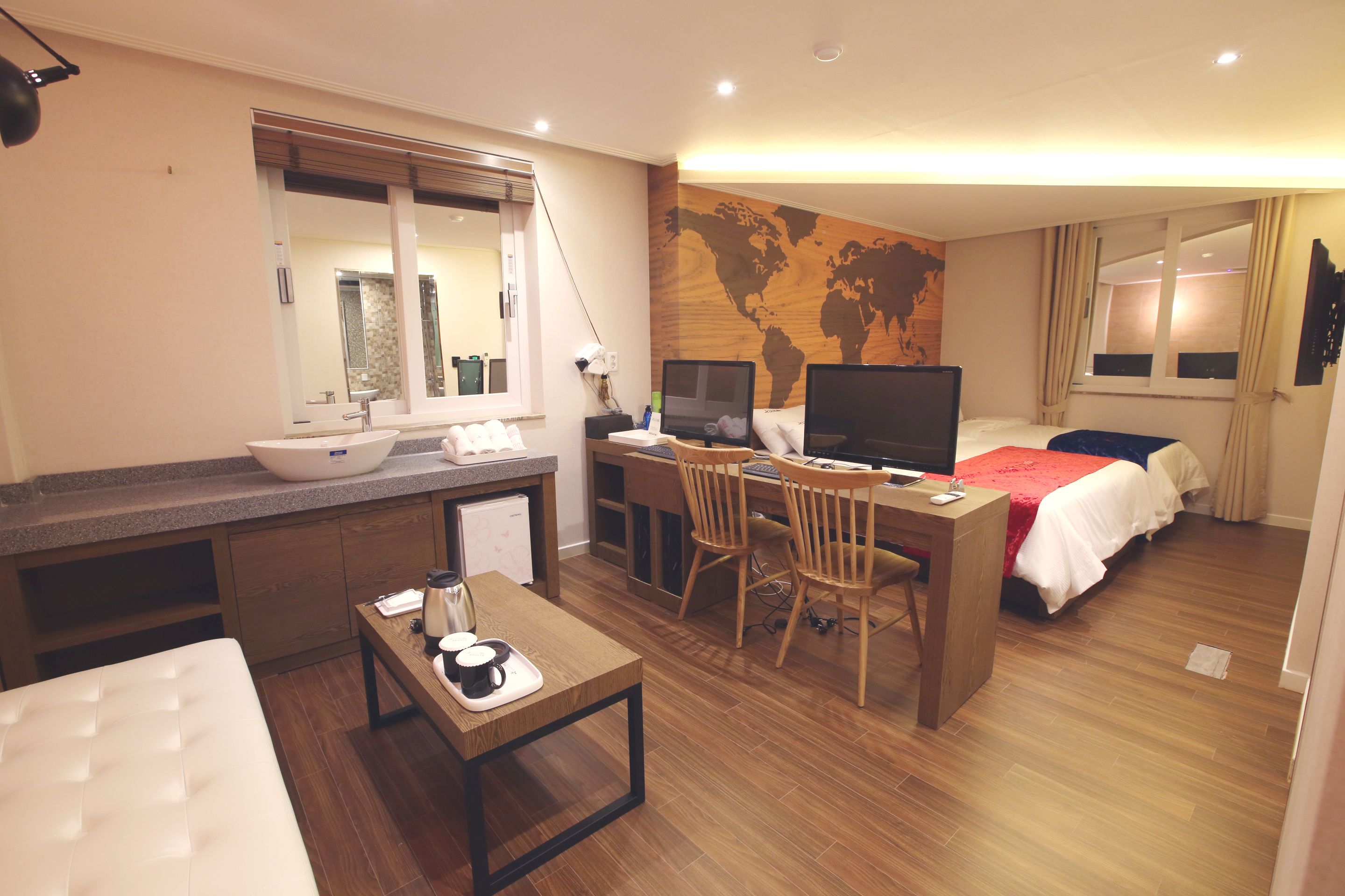 A hotel room with a bed, desk, chair, and a large world map on the wall.