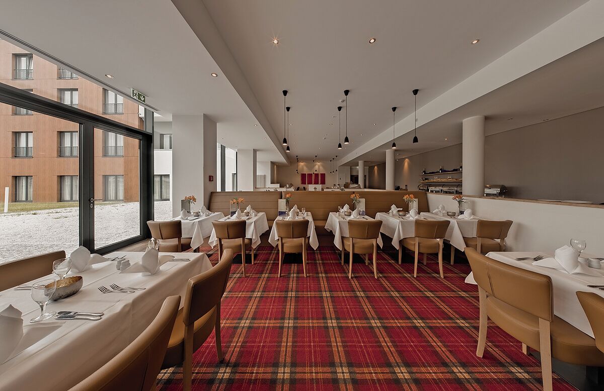 Ein Restaurant mit gedeckten Tischen, einem karierten Teppich und Blick auf Gebäude.