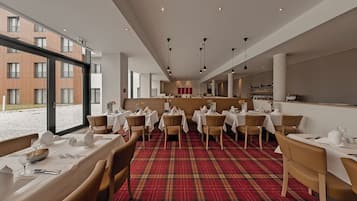A restaurant with tables set for dining, a plaid carpet, and a view of buildings outside.