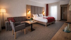 A hotel room with a bed, a sofa, a small table, and a lamp.