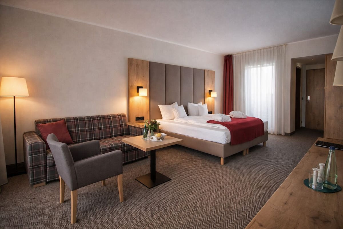Una habitación de hotel con cama, sofá, una mesita y una lámpara.