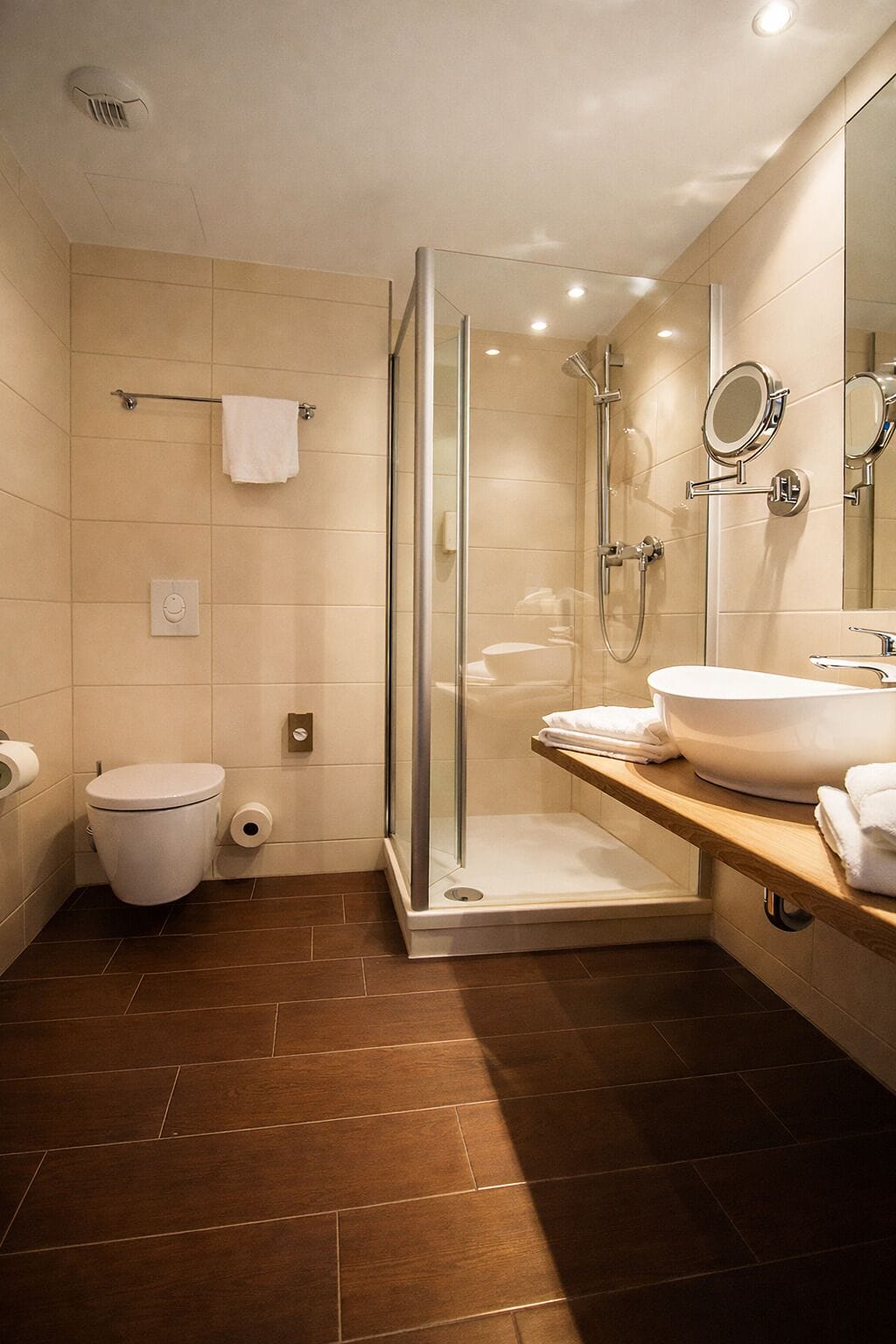 A modern bathroom with a glass-enclosed shower, a white toilet, and a vanity with a large mirror and sink.