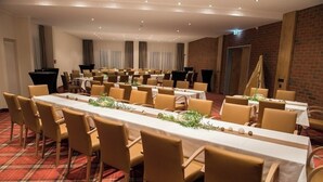 A conference room with long tables and chairs, a red plaid carpet, and brick walls.