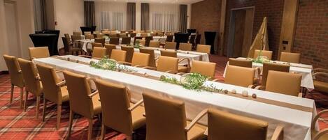 A conference room with long tables and chairs, a red plaid carpet, and brick walls.