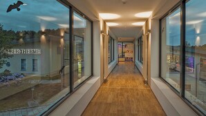 A modern corridor with glass walls, wooden flooring, and ceiling lights.