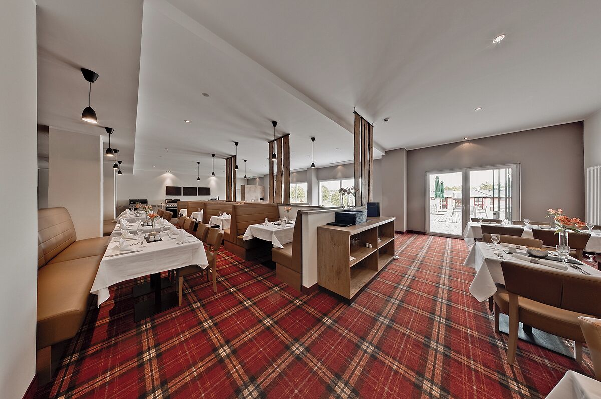 A modern dining area with a red plaid carpet, long tables set for dining, and a mix of seating options including sofas and chairs.