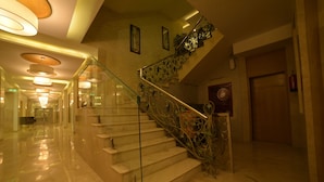 A marble-floored corridor with a glass railing staircase. - Hotel Babylon Inn (Raipur)