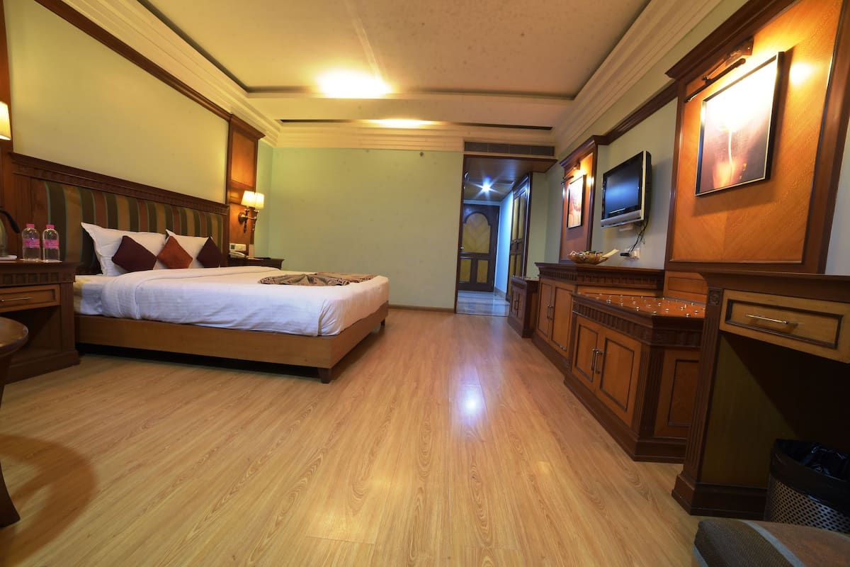 Habitación de hotel con una cama de madera, televisor, escritorio y baño a la vista a través de una puerta abierta.