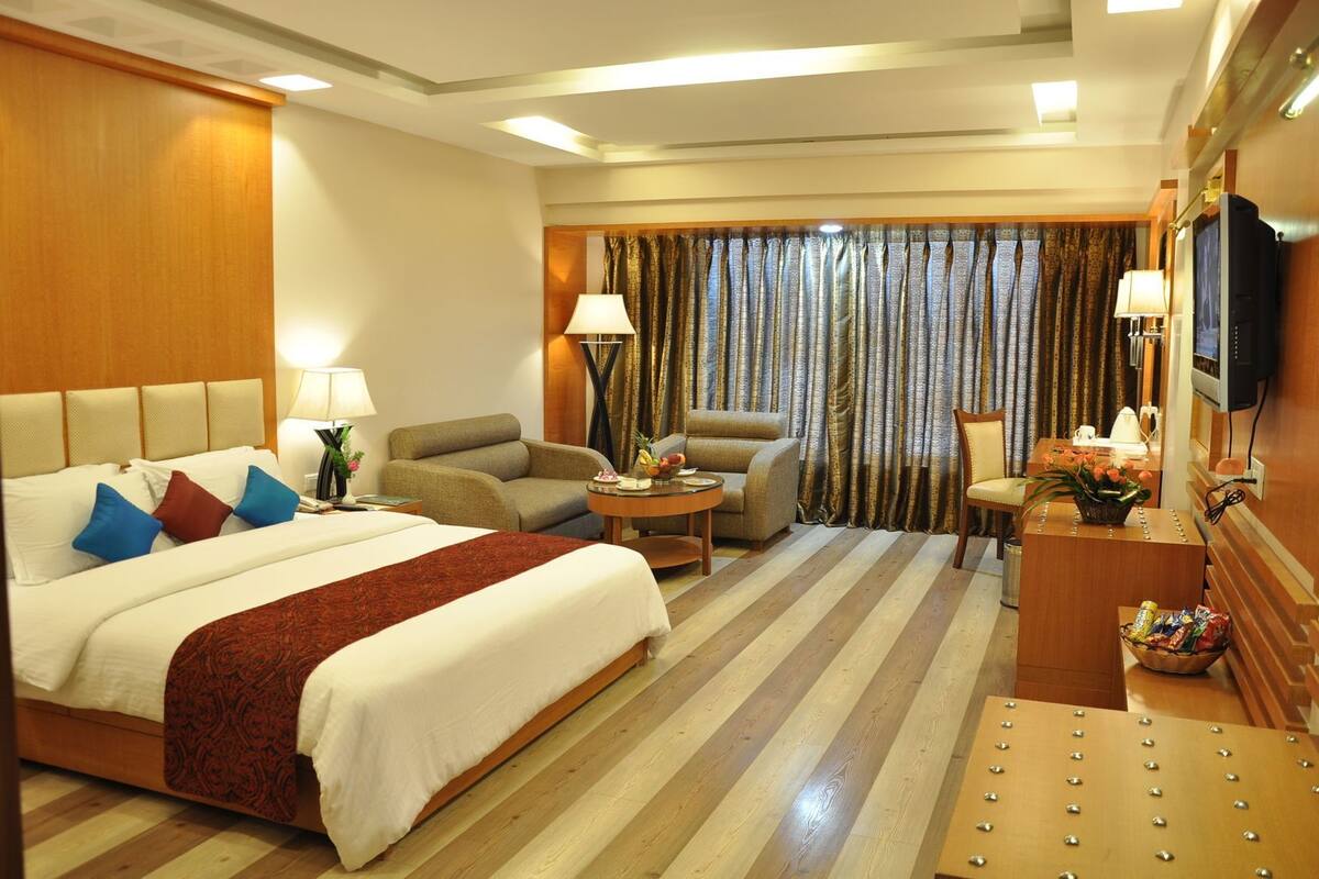 Habitación de hotel con una cama grande, dos sillones, una mesita, televisor y ventana con cortinas.