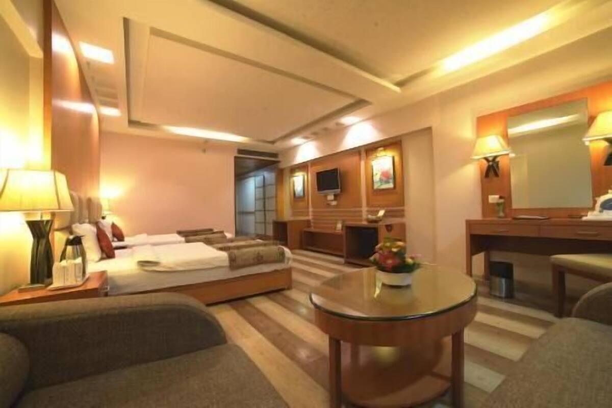 Una habitación de hotel con cama, sofá, una mesita redonda, televisor y espejo.