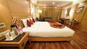 A hotel room with a large bed, wooden flooring, a desk with a coffee maker, and a chair.