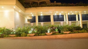 A building with a paved entrance area, multiple windows, and a series of planters with various plants. - Hotel Babylon Inn (Raipur)