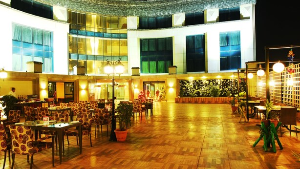 A spacious indoor area with multiple dining tables and chairs, a central open space, and a decorative wall with plants. - Hotel Babylon Inn (Raipur)